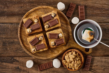 S'mores Blondie with rich buttery base, pockets of melted chocolate and gooey marshmallow, topped with graham cracker crumbs, toasted marshmallows, and Hershey's chocolate for a decadent s'mores treat.